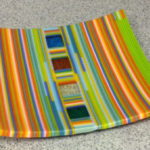 Decorative plate of strips of orange, green, yellow and blue. Item number 108: 9 1/2 by 9 1/2
