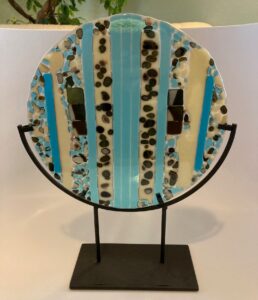 Modern reactive display piece with vanilla and blues and dark greens . Item number 216: 10" round". Price: $45. Metal display additional $20
