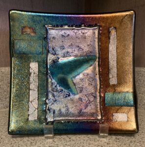 This show stopper art piece is a mixed textured irid plate made up of gold, green, blue, purple, and silver. Item number 234: 8" by 8". Price: $50